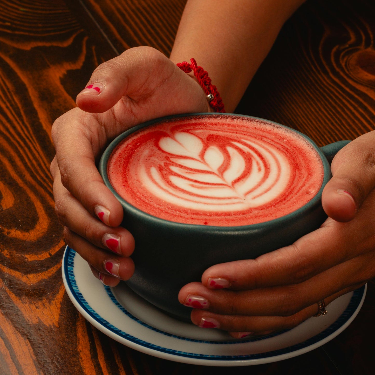 Person holding a cup of beetroot latte with latte art on a wooden table