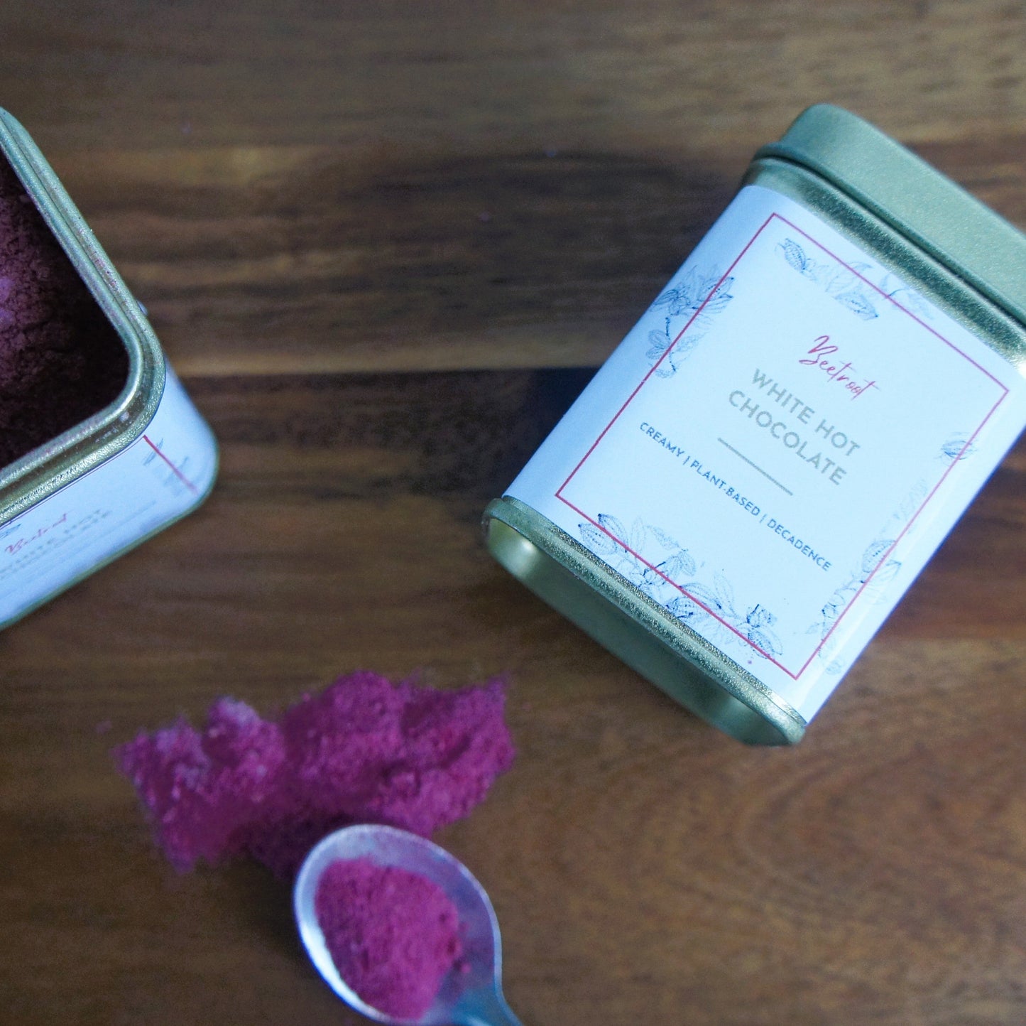 Gold tins with pink beetroot powder on a wooden surface