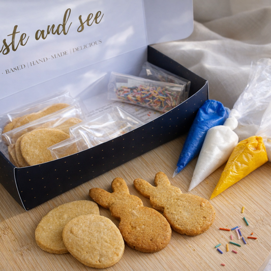 Box of cookies with bunny shapes, piping bags, and sprinkles on a wooden board.