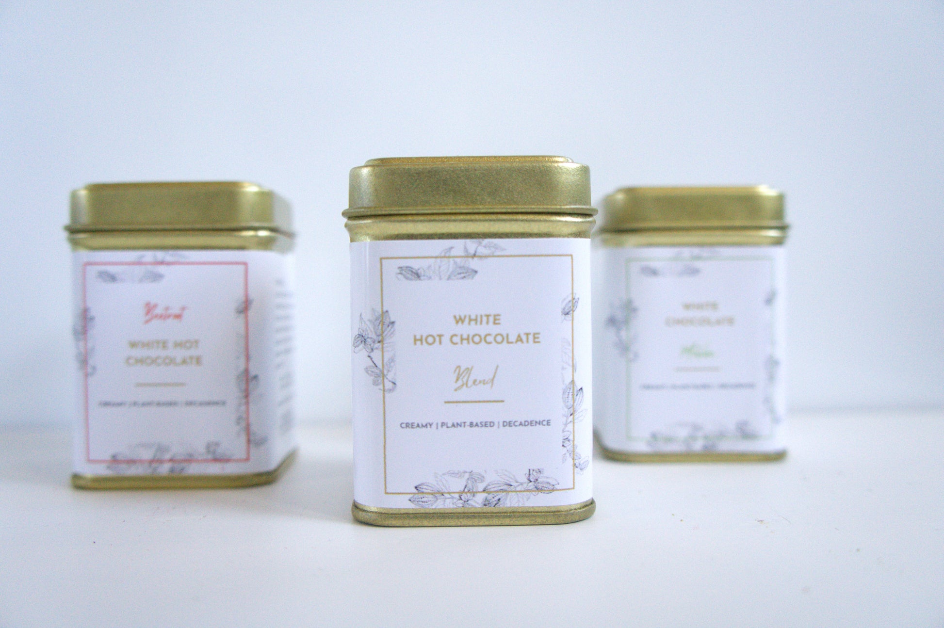 Three tins of vegan white hot chocolate on a light grey background