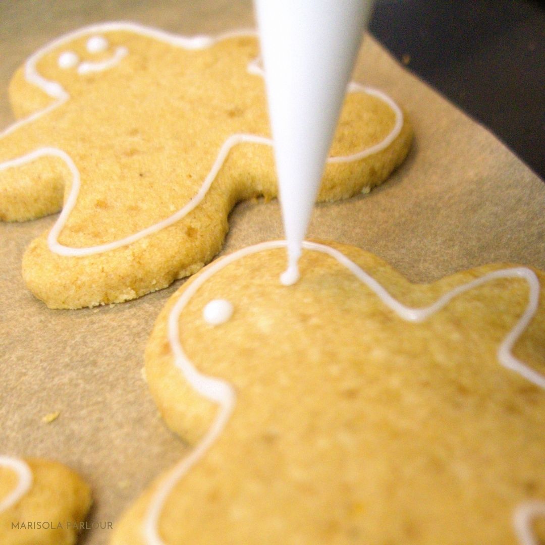 Gingerbread men being decorated with white icing on a baking sheet.