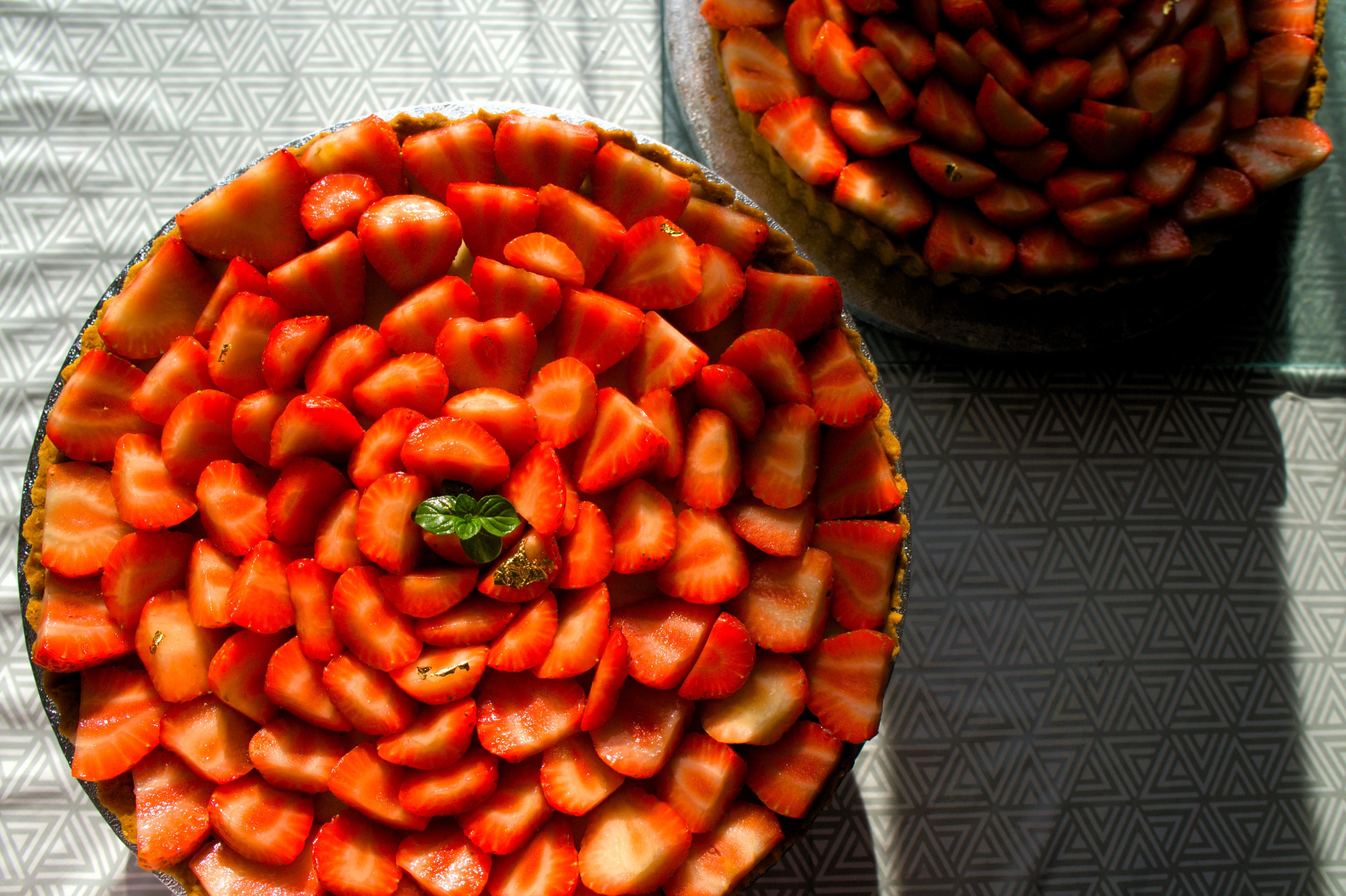 Two strawberry pies on a reflective surface with a geometric patterned background