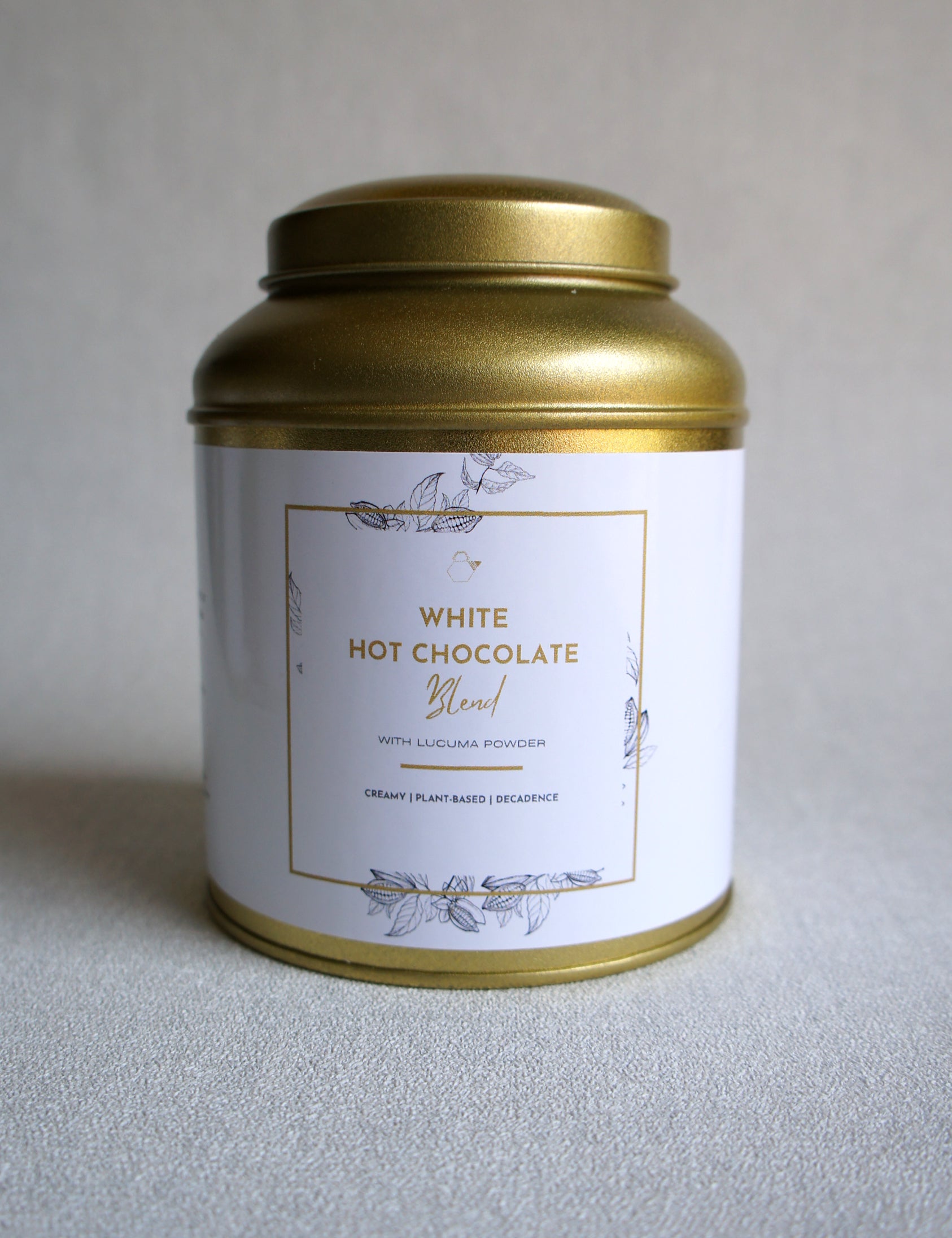 Gold canister of white hot chocolate blend on a light gray background