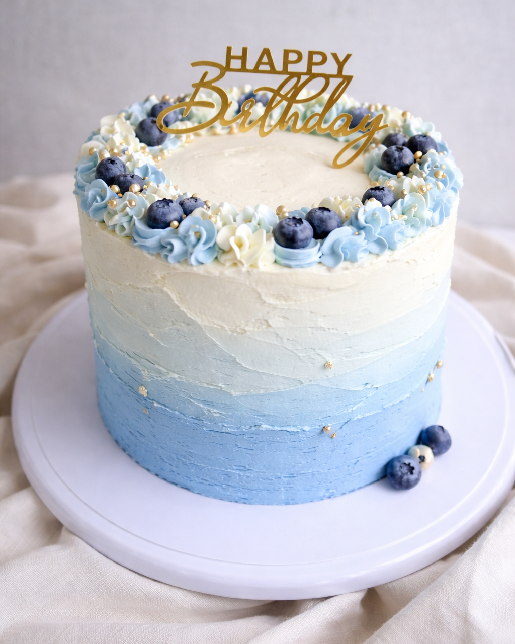 Blue and white birthday cake with blueberries and 'Happy Birthday' topper on a neutral background. Available in Romford