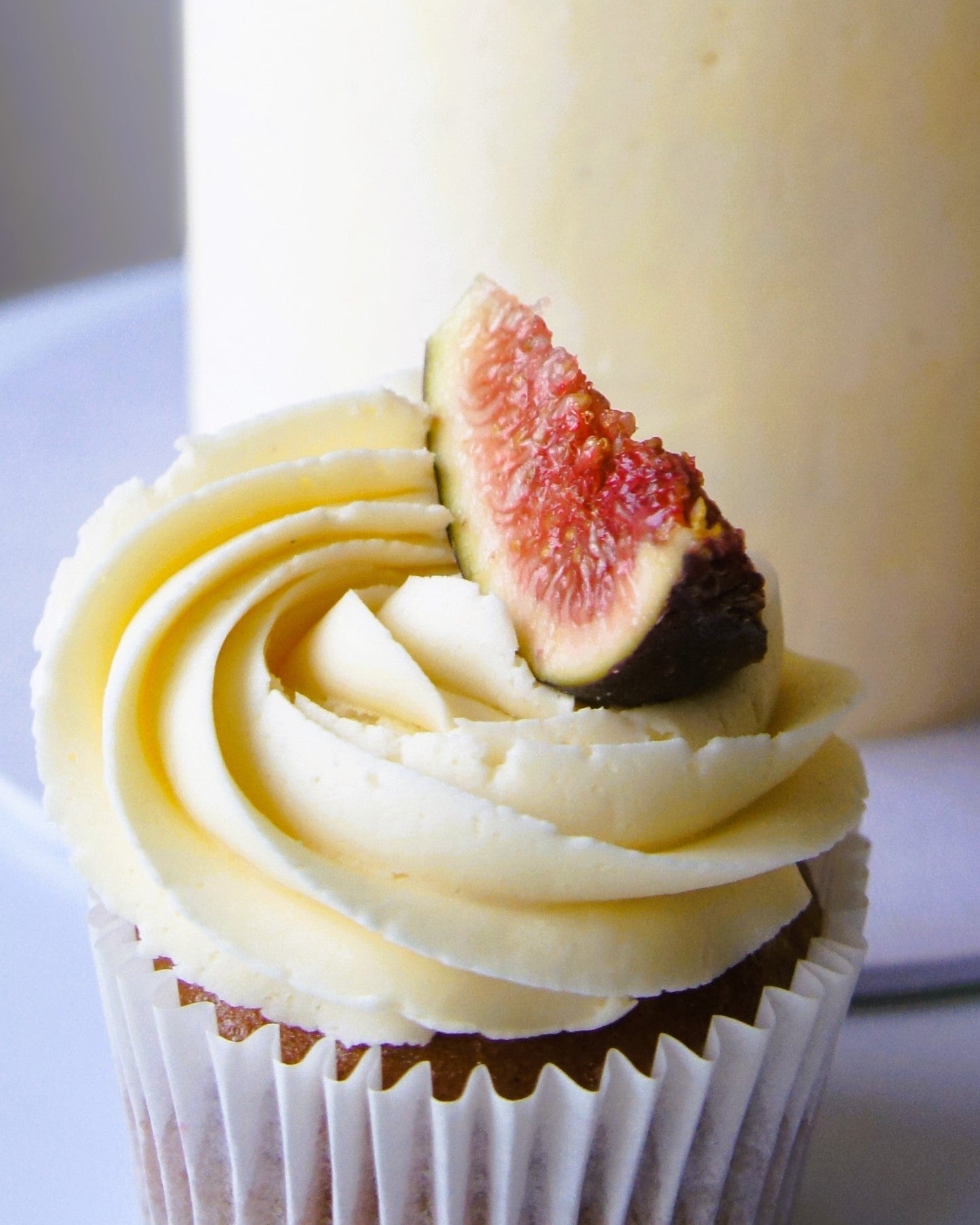 Vegan Cupcake with white frosting and a fig on top, blurred background