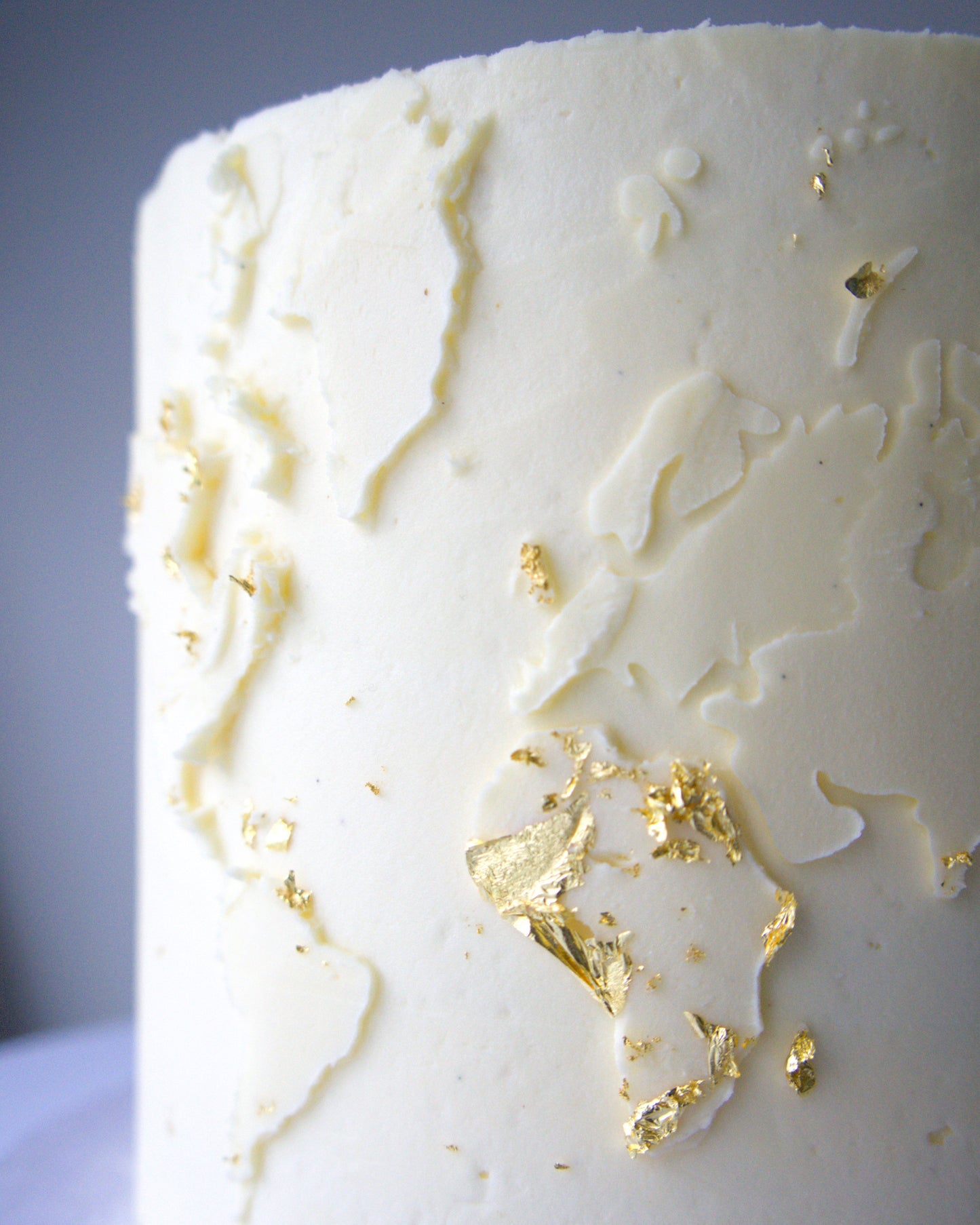 Vegan gluten-free world map cake with textured buttercream and edible gold leaf detail