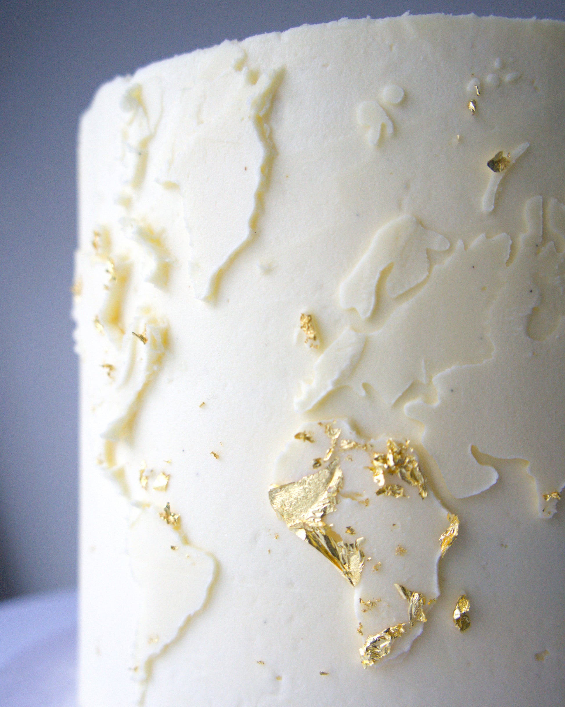 Vegan gluten-free world map cake with textured buttercream and edible gold leaf detail