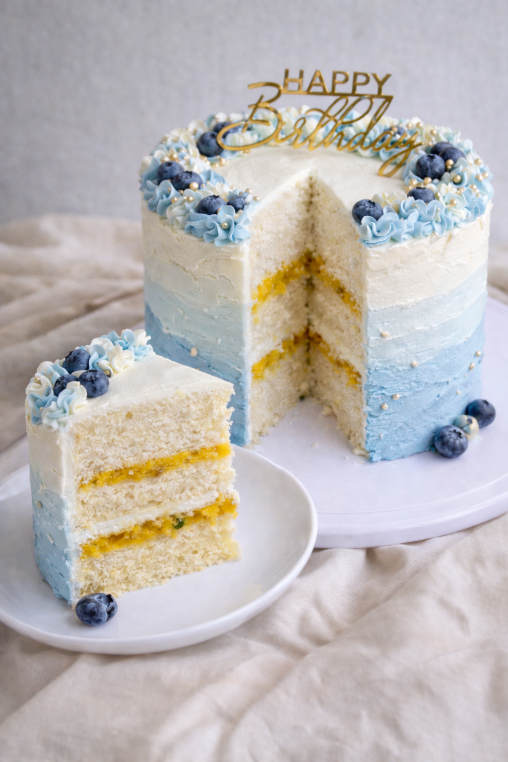 Birthday cake with blue and white layers, blueberries, and a 'Happy Birthday' topper on a neutral background.
